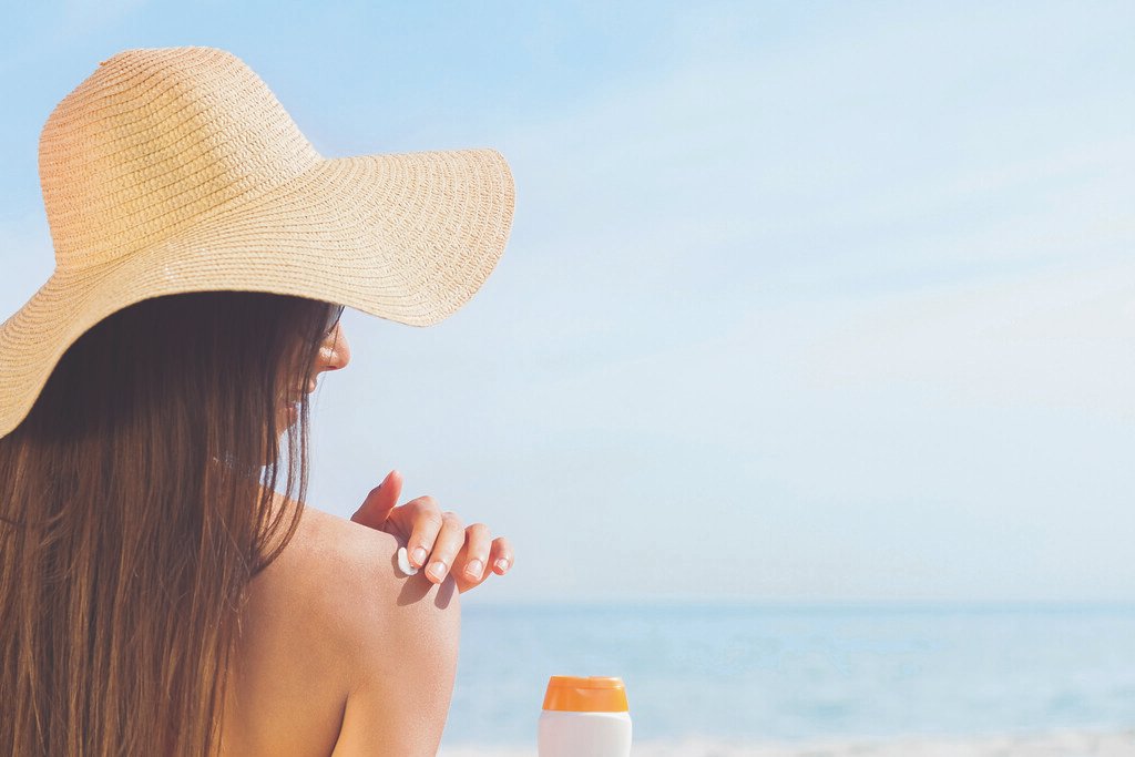 Woman in sunhat applying sunscreen at the beach