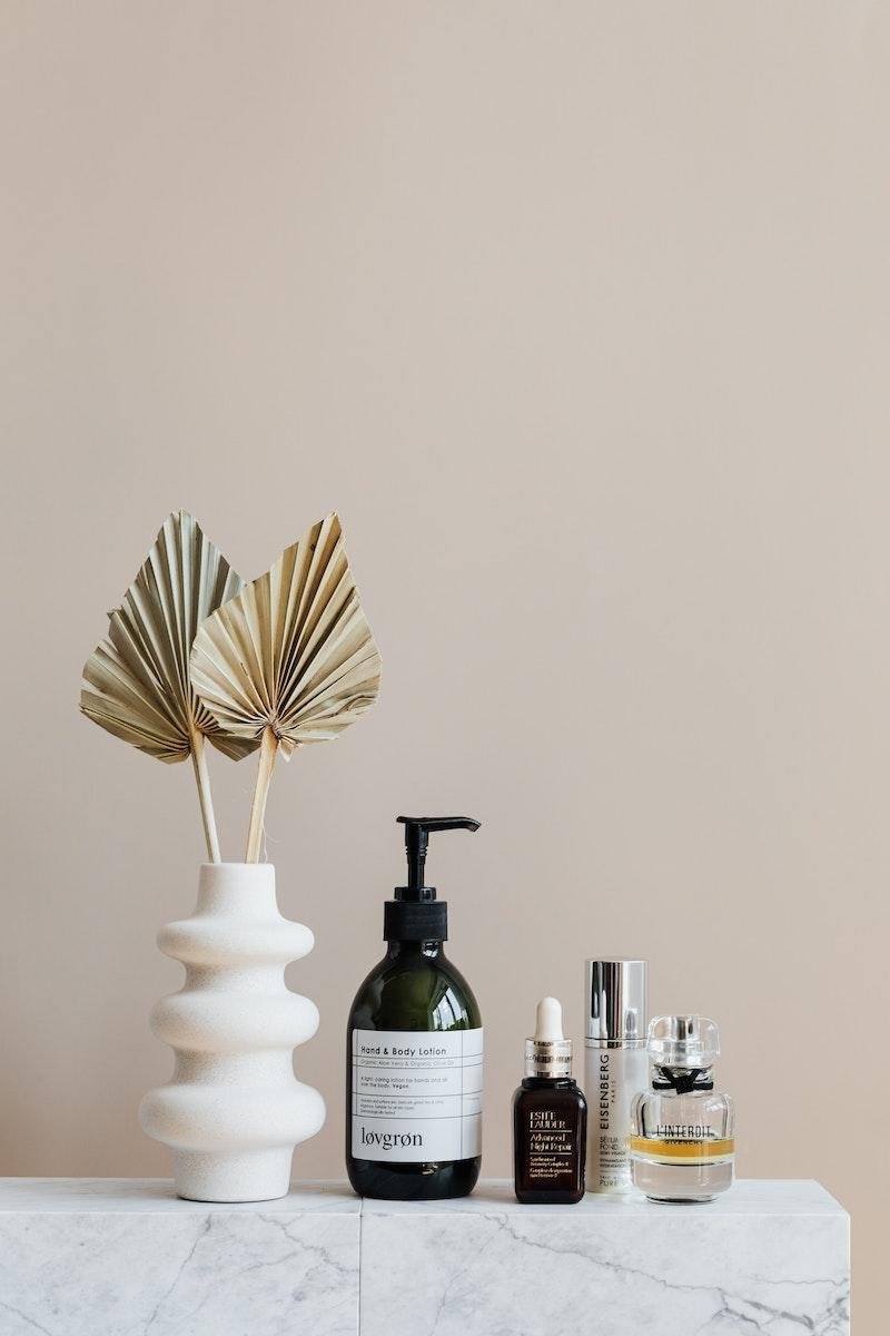 Set of microbiome skincare products near decorative leaves in vase on marble shelf