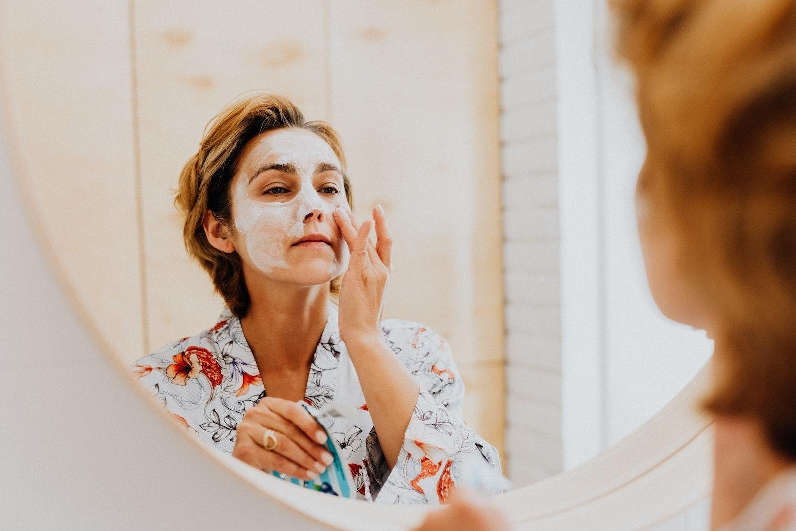 Woman Applying bakuchiol Mask on Her Face in Front of a Mirror