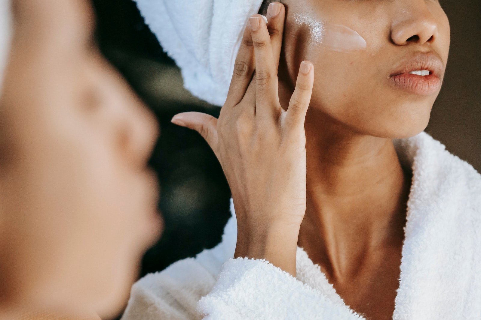 Woman applying moisturizing cream on cheek while reflecting in mirror