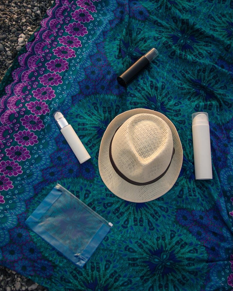 summer skincare products and white fedora on a tapestry background